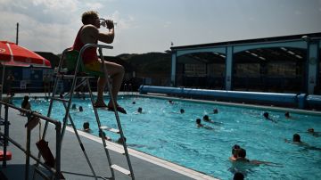 A lifeguard takes a drink as people swim in an outside pool at Hathersage Swimming Pool, west of Sheffield in northern England on July 18, 2022, during an extreme heat wave. Britain could hit 40 Celsius (104 Fahrenheit) for the first time, forecasters said, causing havoc in a country unprepared for the onslaught of extreme heat that authorities said was putting lives at risk. (Photo by Oli SCARFF / AFP) / -- IMAGE RESTRICTED TO EDITORIAL USE - STRICTLY NO COMMERCIAL USE -- (Photo by OLI SCARFF/AFP via Getty Images)