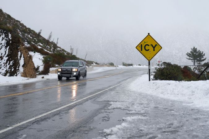 An SUV drives past an icy sign in the San Gabriel Mountains in the Angeles National Forest, California, on February 24, 2023. - Californians more used to flip flops and shorts were wrapping up warm Thursday as a rare winter blizzard, the first in more than 30 years, loomed over Los Angeles, even as the US East Coast basked in summer-like temperatures. (Photo by Allison Dinner / AFP) (Photo by ALLISON DINNER/AFP via Getty Images)