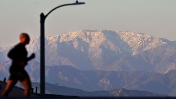 A man jogs in Los Angeles with snow-capped mouthains seen in the distance on March 2, 2023 in Los Angeles, California where a new cold system brought hail and snow to unusually low elevations for the mountains in Southern California. (Photo by Frederic J. BROWN / AFP) (Photo by FREDERIC J. BROWN/AFP via Getty Images)
