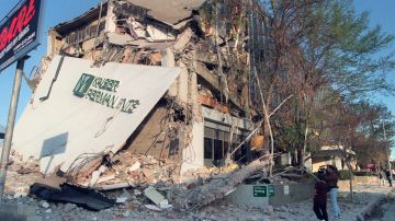 A resident and a cameraman look at damage to the Kaiser Permanente Building following the Northridge earthquake, on January 17, 1994. The earthquake measured 6.6 on the Richter scale and was centered in the San Fernando Valley. (Photo by HAL GARB / AFP) (Photo by HAL GARB/AFP via Getty Images)