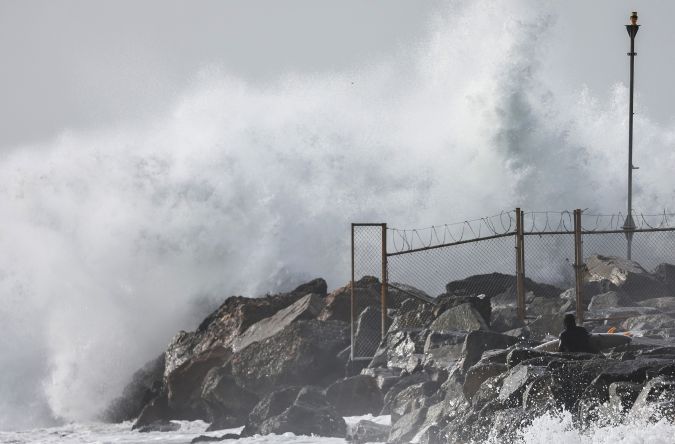 EL SEGUNDO, CALIFORNIA - DECEMBER 29: A surfer (LOWER R) waits to enter the water from a jetty as large waves break near the beach on December 29, 2023 in El Segundo, California. Dangerous surf churned up by storms in the Pacific is impacting much of California’s coastline with coastal flooding possible in some low-lying areas. (Photo by Mario Tama/Getty Images)