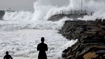 EL SEGUNDO, CALIFORNIA - DECEMBER 29: Surfers look on near a jetty as large waves break near the beach on December 29, 2023 in El Segundo, California. Dangerous surf churned up by storms in the Pacific is impacting much of California’s coastline with coastal flooding possible in some low-lying areas. (Photo by Mario Tama/Getty Images)
