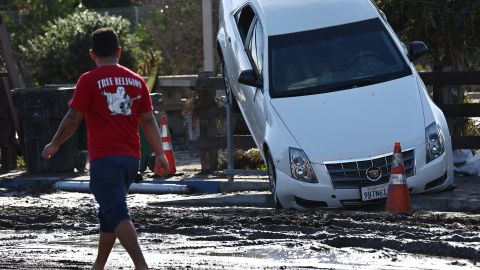 SAN DIEGO, CALIFORNIA - JANUARY 23: A person stands near a vehicle moved by flooding that remains lodged on a fence the day after an explosive rainstorm deluged areas of San Diego County on January 23, 2024 in San Diego, California. The intense rains forced dozens of rescues while flooding roadways and homes and knocking out electricity for thousands of residents. (Photo by Mario Tama/Getty Images)