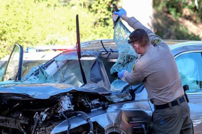 A law enforcement officer looks over a damaged vehicle following a rollover accident involving golfer Tiger Woods, Tuesday, Feb. 23, 2021, in the Rancho Palos Verdes suburb of Los Angeles. Woods suffered leg injuries in the one-car accident and was undergoing surgery, authorities and his manager said. (AP Photo/Ringo H.W. Chiu)