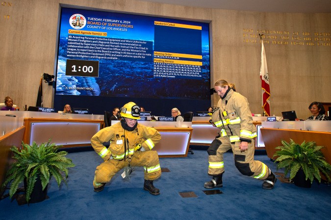 Las bomberos del condado de Los Ángeles, Emily Fuller y Siene Freeman, demuestran cómo el equipo de protección diseñado para hombres restringe su movimiento. (Oficina supervisora Janice Hahn)