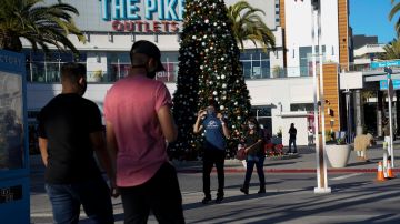 Shoppers wearing face masks walk past a Christmas tree at The Pike Outlets Saturday, Dec 26, 2020, in Long Beach, Calif. (AP Photo/Ashley Landis)