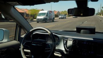 A Waymo minivan moves along a city street as an empty driver's seat and a moving steering wheel drive passengers during an autonomous vehicle ride, Wednesday, April 7, 2021, in Chandler, Ariz. Waymo, a unit of Google parent Alphabet Inc., is one of several companies testing driverless vehicles in the U.S. But it's the first offering lifts to the public with no humans at the wheel who can take over in sticky situations. (AP Photo/Ross D. Franklin)