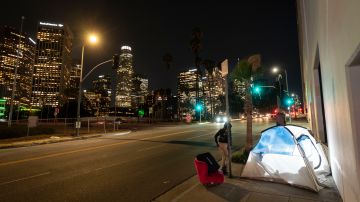In this photo illuminated by an off-camera flash, a woman walks past a homeless person's tent with a chair in downtown Los Angeles, Thursday, Feb. 16, 2023. A new study by the University of California, San Francisco shows that homeless people in California were struggling with poor health and deep poverty before becoming homeless. The study released Tuesday, June 20, by the Benioff Homelessness and Housing Initiative aims to provide a comprehensive picture of adult homelessness in a state that has 30% of the country's homeless. (AP Photo/Jae C. Hong)
