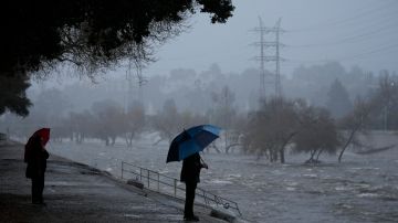 A couple walks on the edge of the Los Angeles River, carrying stormwater downstream Sunday, Feb. 4, 2024, in Los Angeles. The second of back-to-back atmospheric rivers battered California, flooding roadways and knocking out power to hundreds of thousands and prompting a rare warning for hurricane-force winds as the state braced for what could be days of heavy rains. (AP Photo/Damian Dovarganes)