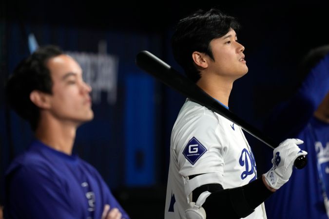 Los Angeles Dodgers designated hitter Shohei Ohtani, right, stands in the dugout with Dodgers manager of performance operations and interpreter Will Ireton during the first inning of a baseball game against the San Diego Padres at the Gocheok Sky Dome in Seoul, South Korea Thursday, March 21, 2024, in Seoul, South Korea. (AP Photo/Lee Jin-man)