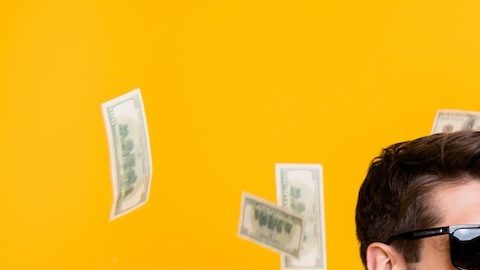 Foto de un joven tirando dólares y sonriendo sobre un fondo amarillo.