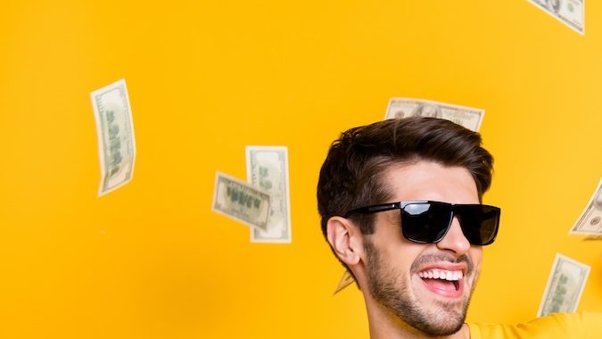 Foto de un joven tirando dólares y sonriendo sobre un fondo amarillo.