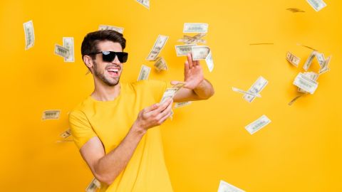Foto de un joven tirando dólares y sonriendo sobre un fondo amarillo.