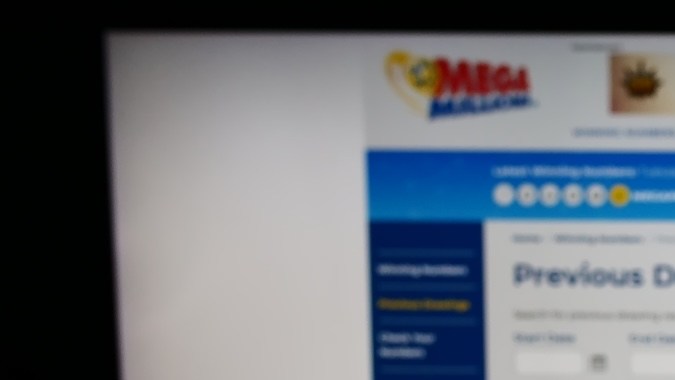 Persona que sostiene un teléfono celular con el logotipo de la lotería estadounidense Mega Millions en la pantalla frente a la página web.