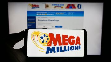 Persona que sostiene un teléfono celular con el logotipo de la lotería estadounidense Mega Millions en la pantalla frente a la página web.