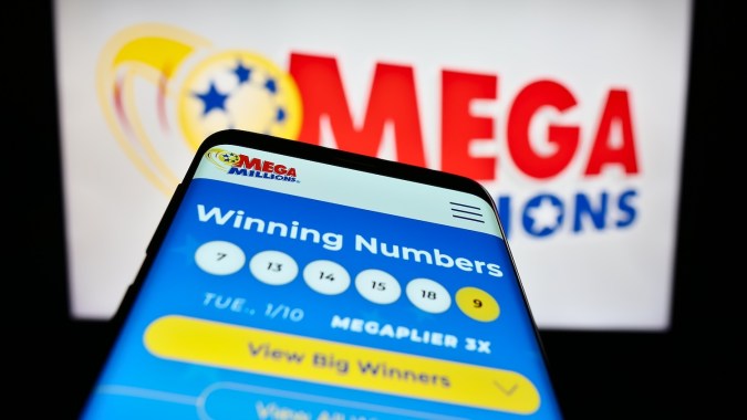 Smartphone con sitio web del juego de lotería estadounidense Mega Millions en la pantalla frente al logotipo
