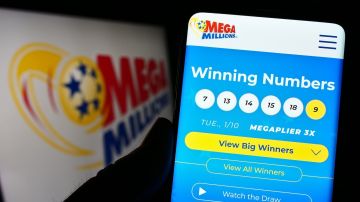Persona que sostiene el teléfono celular con la página web de la lotería estadounidense Mega Millions en la pantalla frente al logotipo.