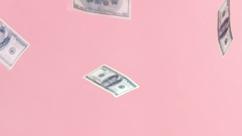 Alegre mujer parada bajo una lluvia de dinero sobre fondo rosa.