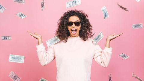 Alegre mujer parada bajo una lluvia de dinero sobre fondo rosa.