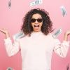 Alegre mujer parada bajo una lluvia de dinero sobre fondo rosa.