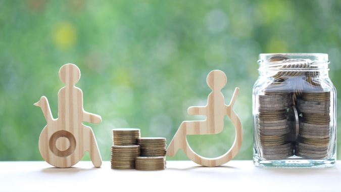 Hombres de madera en sillas de ruedas y dinero en monedas sobre fondo verde natural.