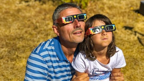 Padre e hija, familia viendo el eclipse solar con gafas especiales en un parque.