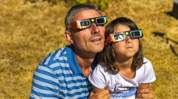 Padre e hija, familia viendo el eclipse solar con gafas especiales en un parque.