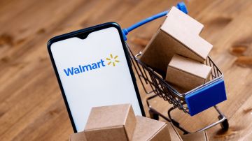 Smartphone con logo de Walmart en pantalla, carrito de compras y paquetes.