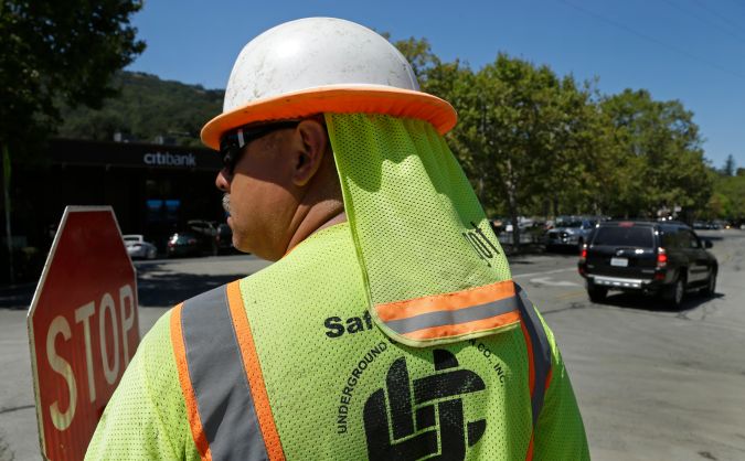 A construction worker wears a neck cover while directing traffic on Monday, Aug. 28, 2017, in Orinda, Calif. Temperatures in excess of 100 degrees continue for a third day in inland areas of the Bay Area. (AP Photo/Ben Margot)