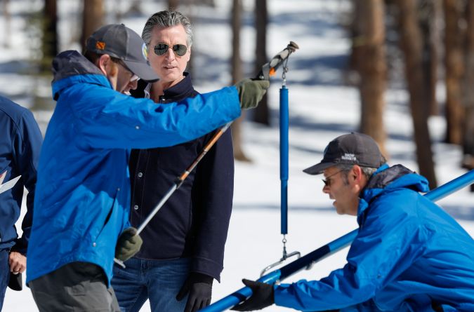 Gov. Gavin Newsom watches as Water Engineers Andy Reising, right, and Anthony Burdock, part of the California Department of Water Resources Snow Surveys and Water Supply Forecasting Unit, conduct the fourth media snow survey of the 2024 season at Phillips Station in the Sierra Nevada. The survey is held approximately 90 miles east of Sacramento off Highway 50 in El Dorado County.  Photo taken April 2, 2024.     Fred Greaves / California Department of Water Resources