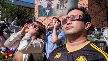 Jennifer Delgado (i), Andrew Areola y Alistaire Roleda ven el eclipse solar afuera del Centro de Ciencias de California en Los Ángeles.