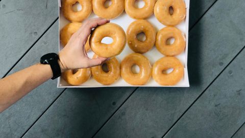 Una mano toma una dona original y fresca de Krispy Kreme.