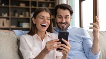 Una joven pareja familiar llena de alegría mirando la pantalla del teléfono por el bono recibido al abrir una cuenta bancaria.