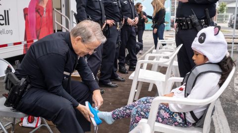 Un oficial ayuda a probarse unos zapatos a una estudiante de la escuela Bassett Street Elementary School