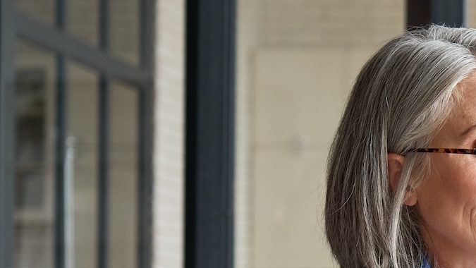 Mujer mayor seria en casa en el sofá sosteniendo un teléfono móvil.