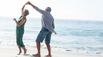 Una pareja mayor bailando en la playa en un día soleado.