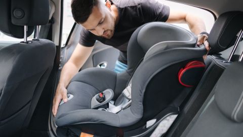 El hombre instala un asiento infantil en el asiento trasero del coche.