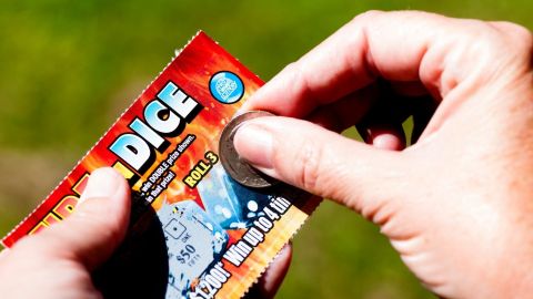 Primer plano de unas manos rascando con una moneda un raspadito de lotería.