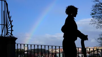 A young woman rides an electric scooter as the sun comes out and a rainbow appears in the sky following a spring rain shower, in Lisbon, Tuesday, March 26, 2024. (AP Photo/Armando Franca)
