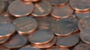 Una alcancía blanca muy pequeña sentada sobre un paisaje de monedas de un centavo nuevas y viejas.