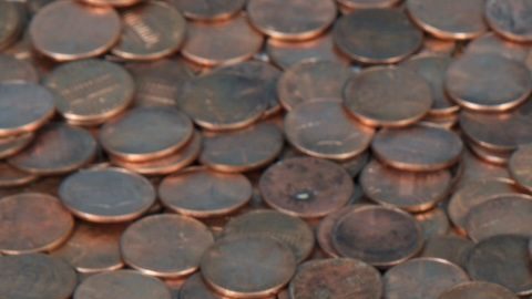 Una alcancía blanca muy pequeña sentada sobre un paisaje de monedas de un centavo nuevas y viejas.