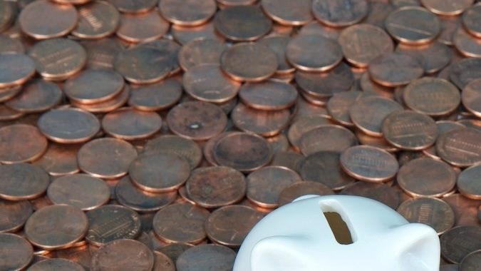 Una alcancía blanca muy pequeña sentada sobre un paisaje de monedas de un centavo nuevas y viejas.