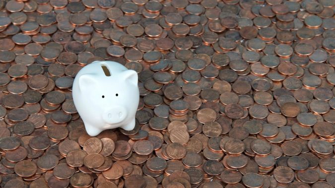 Una alcancía blanca muy pequeña sentada sobre un paisaje de monedas de un centavo nuevas y viejas.