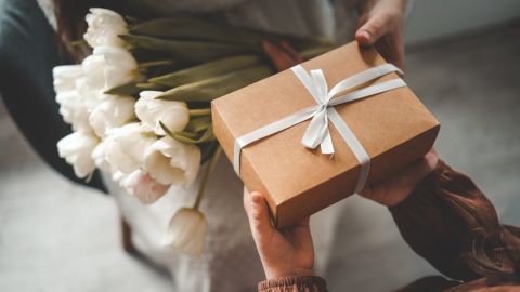 Manos de niño entregando un regalo y flores por el Día de la Madre.