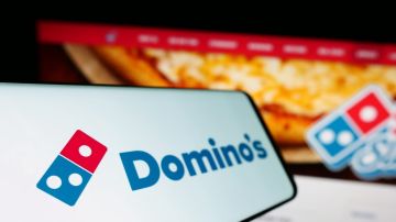 Smartphone con el logotipo de la cadena de restaurantes estadounidense Domino's Pizza, frente al sitio web de la empresa.