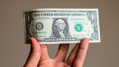 Mano sosteniendo un billete de dólar estadounidense.