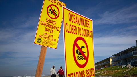 A couple walk along the beach as signs warn of contaminated water Wednesday, Dec. 12, 2018, at Imperial Beach, Calif. Authorities say more than 6 million gallons (22 million liters) a day of raw sewage has been spilling into Mexico's Tijuana River since Monday night, and the waste is flowing north into Southern California waters. Swimmers and surfers are urged to stay out of the water at some San Diego County beaches. (AP Photo/Gregory Bull)