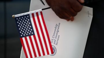 Maweya Babekir, of Iowa City, Iowa, holds a flag before taking the Oath of Allegiance during a drive-thru naturalization ceremony at Principal Park, Friday, June 26, 2020, in Des Moines, Iowa. The U.S. has resumed swearing in new citizens, but the traditional oath ceremonies aren't the same because of COVID-19. Thousands of people are participating in drive-up ceremonies intended to preserve social distancing. Now a budget crisis at the citizenship agency is threatening to stall ceremonies again. (AP Photo/Charlie Neibergall)