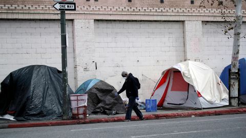 FILE - In this March 20, 2020 file photo a man covers his face with a mask as he walks past tents on skid row, in Los Angeles. A fed-up federal judge says last week's rainstorm created "extraordinarily harsh" conditions for homeless residents of Los Angeles and he has ordered city officials to meet with him this week at a Skid Row shelter to discuss how to address the worsening crisis of people living on the streets. (AP Photo/Marcio Jose Sanchez,File)