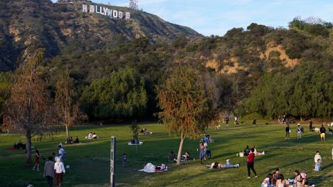 People enjoy the hot weather at the Lake Hollywwod Park as workers transform the iconic Hollywood sign to read "Rams House" in Los Angeles on Monday, Feb. 14, 2022. The Hollywood Chamber of Commerce and the Hollywood Sign Trust allowed for making the change to celebrate the Los Angeles Rams' Super Bowl championship. The altered sign is expected to stay up through Wednesday. (AP Photo/Damian Dovarganes)